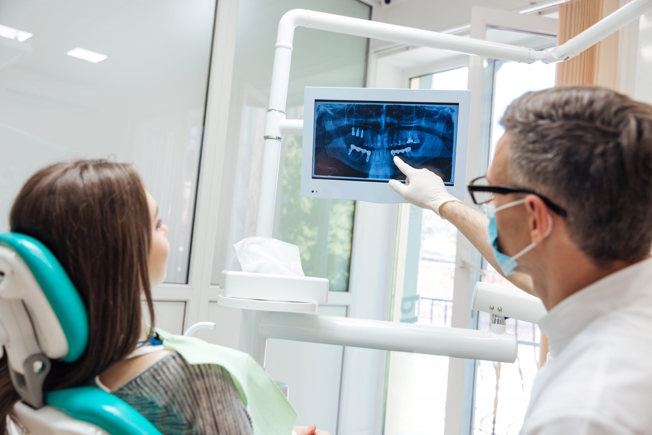 Dentist pointing out something on an x-ray to the patient who is sitting in a dental chair