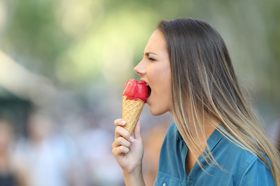 Woman cringing as she takes a bite of red ice cream on a cone.