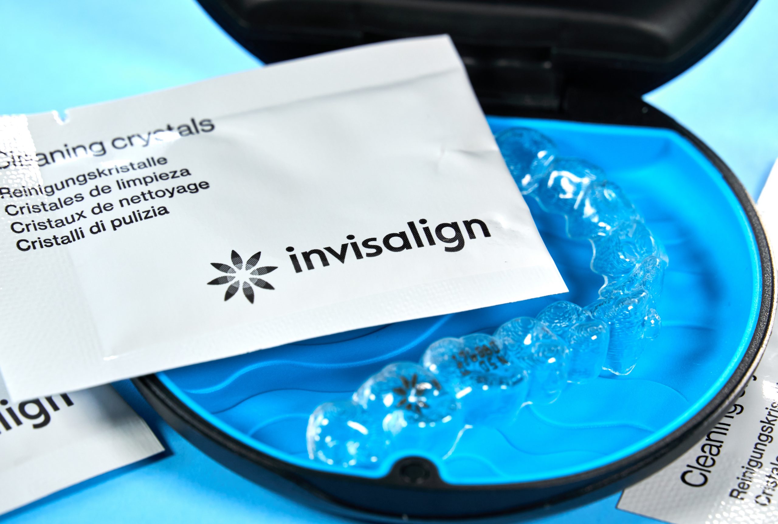 White packet of Invisalign cleaning crystals on top of the clear aligners which are in their blue case