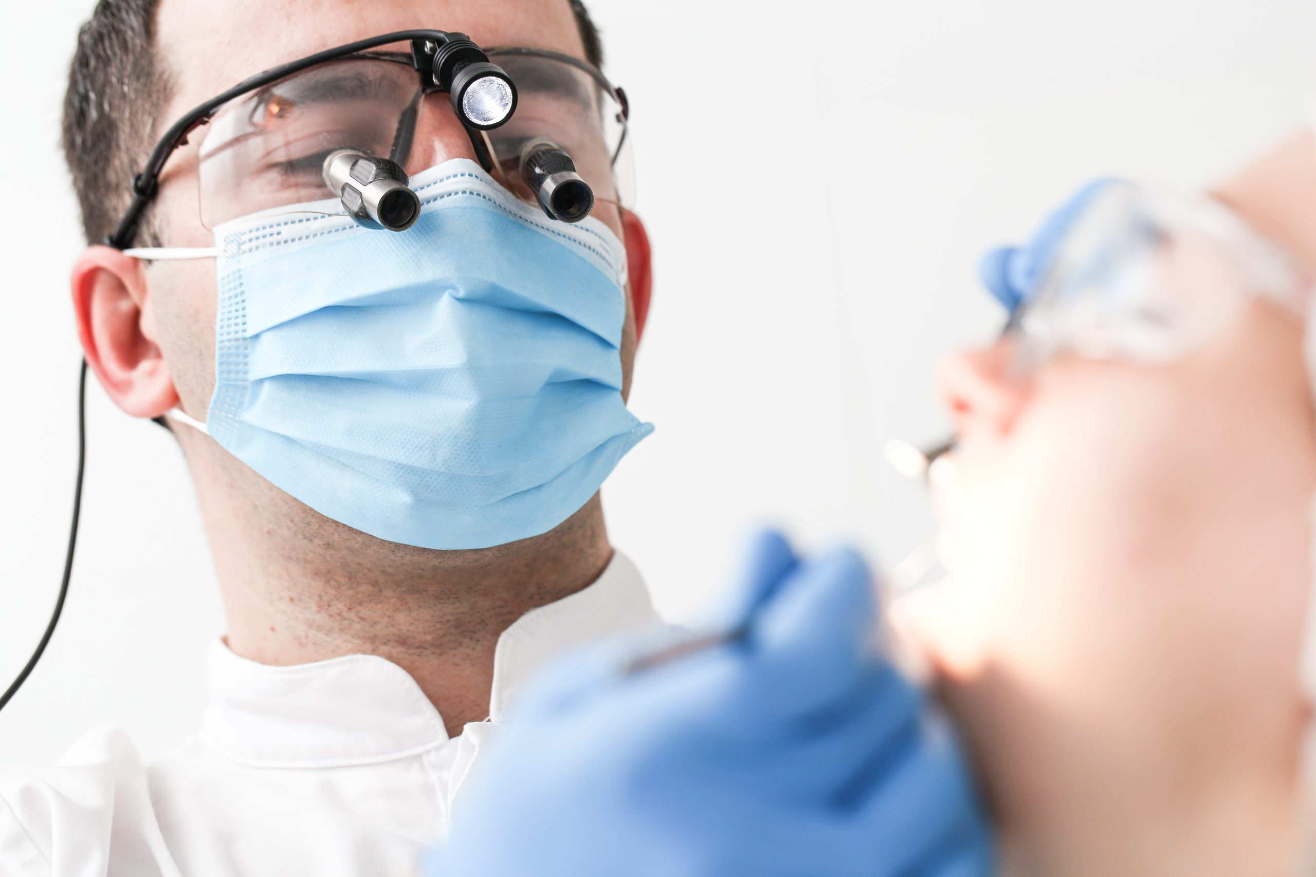 A dentist with dental loupes looking down into a patient's mouth.