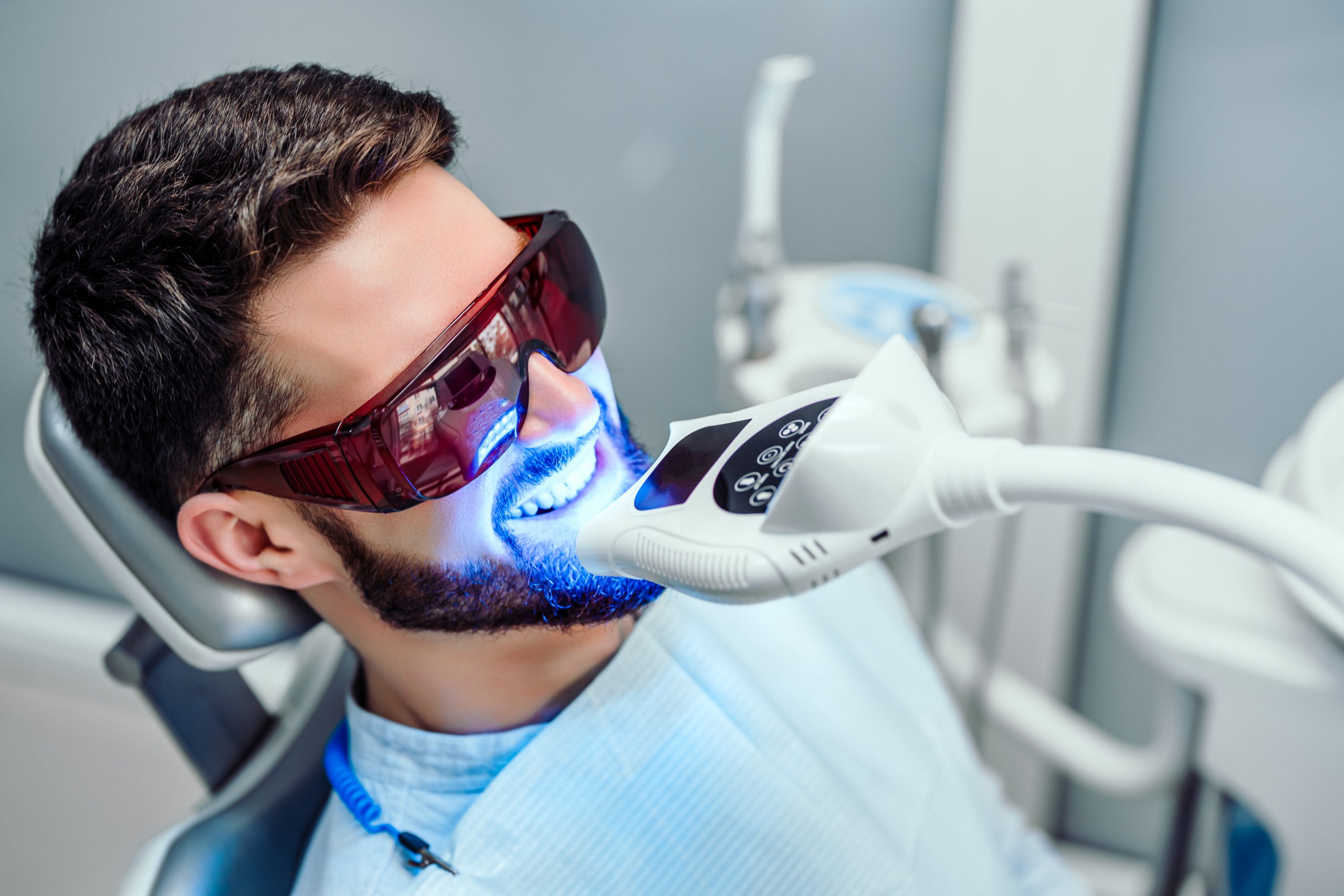Patient sitting in dental chair wearing eye protection while a light is shining on their teeth to activate the whitening chemicals.